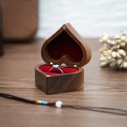 Boîte à bijoux en bois de noyer en forme de cœur ouverte, avec doublure rouge et une bague argentée.