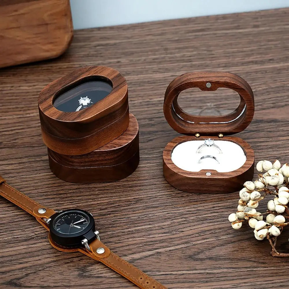 Deux boîtes à bijoux ovales en bois foncé sur une table en bois. L'une est fermée, l'autre ouverte et contient deux bagues.