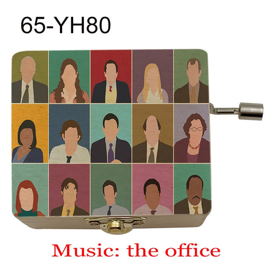 Boîte à musique en bois clair avec manivelle métallique et personnages de la série The Office sur le couvercle.