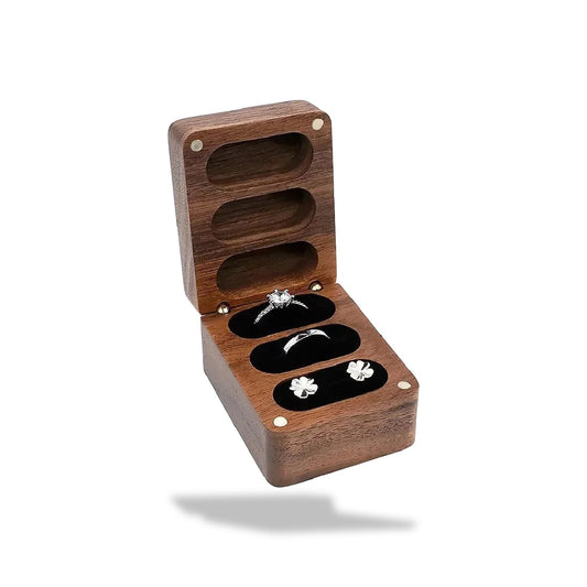 Boîte à bagues en bois de noyer foncé, ouverte, avec trois fentes noires contenant une bague et une paire de boucles d'oreill