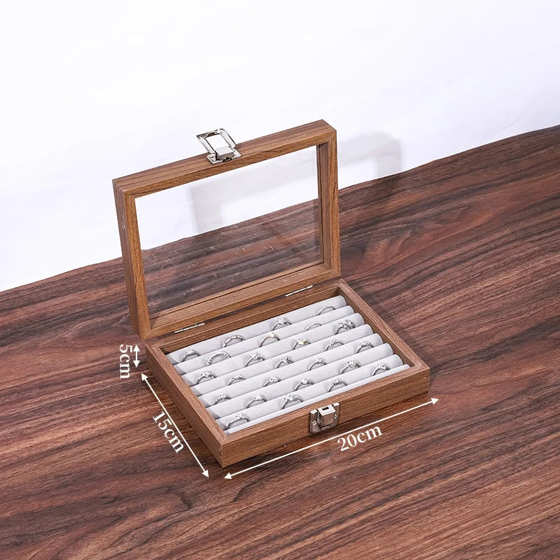 Boîte à bijoux en bois de noyer marron avec couvercle vitré ouvert et 18 emplacements pour bagues sur fond gris.