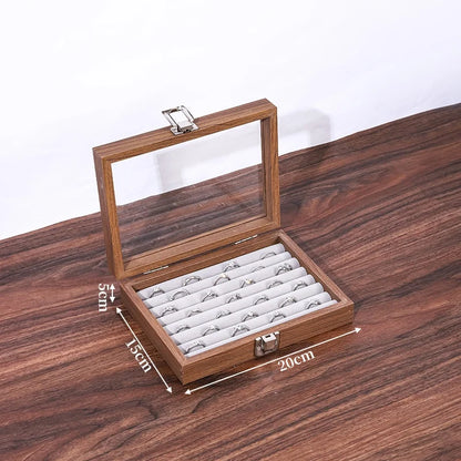 Boîte à bijoux en bois de noyer marron avec couvercle vitré ouvert et 18 emplacements pour bagues sur fond gris.