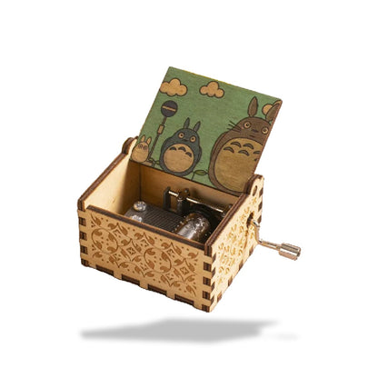 Boîte à musique en bois clair avec motifs gravés, couvercle ouvert illustré de Totoro et amis sur fond vert.