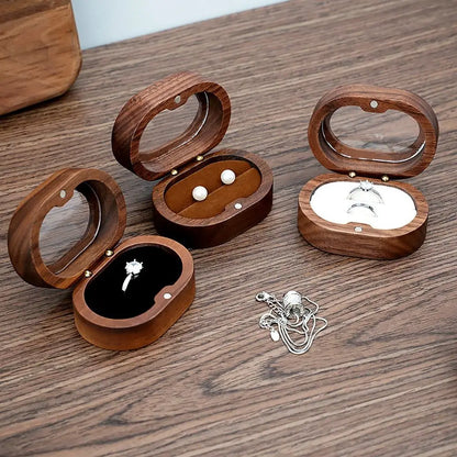 Trois boîtes à bijoux ovales en bois ouvertes sur une table, avec des bijoux à l'intérieur.