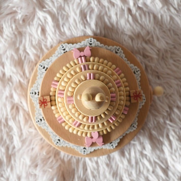 Boîte à musique en bois clair, en forme de gâteau d'anniversaire. Détails roses, rubans et motifs dentelle blanche.