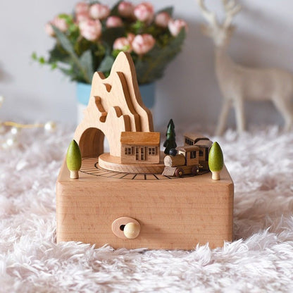 Boîte à musique en bois de hêtre, représente une maison, des arbres et un train en rotation devant une montagne.
