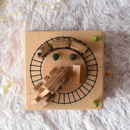 Boîte à musique carrée en hêtre, avec un train en bois gravé tournant sur des rails noirs et des accessoires.