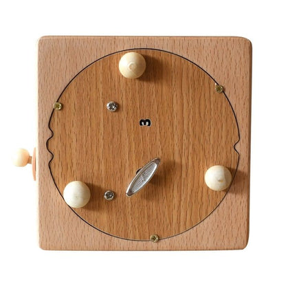 Boîte à musique carrée en hêtre, face avant vue de dessus. Cadran en bois avec manivelle et quatre billes en bois claires.